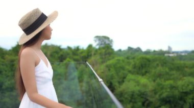 Balkonda hasır şapkalı güzel Asyalı bir kadının görüntüleri.