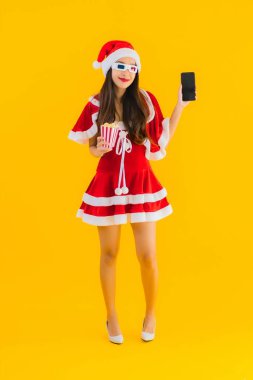 Güzel bir Asyalı kadın portresi patlamış mısır ve 3D gözlüklü noel şapkası takıyor sarı izole edilmiş arka planda film izlemeye hazır.