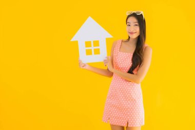 Güzel genç Asyalı kadın sarı izole arka planda ev ya da ev tabelasını gösteriyor.