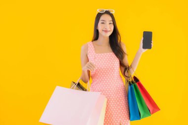 Renkli alışveriş çantalı güzel Asyalı kadın akıllı cep telefonu ve sarı izole edilmiş arka planda kredi kartı.