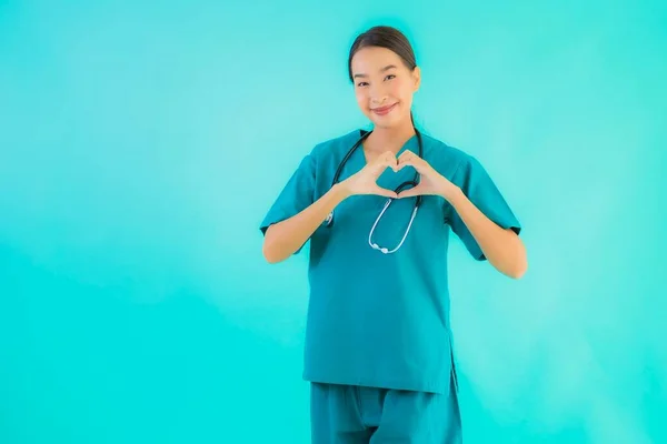 ポートレート美しい若いアジアの医師の女性幸せな笑顔ショーハート形のために仕事で病院やクリニック上の青隔離された背景 — ストック写真