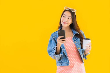 Kahve fincanı ve sarı izole edilmiş arka planda akıllı cep telefonlu güzel Asyalı kadın portresi.