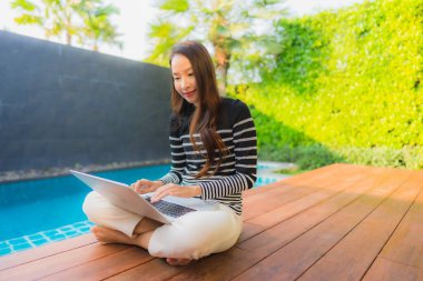 Genç Asyalı bir kadının portresi oteldeki yüzme havuzunda dizüstü bilgisayar kullanıyor.