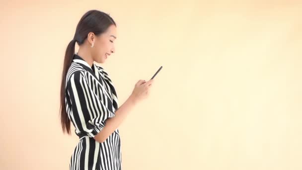 用黄色隔离智能手机拍摄的身穿条纹西装的漂亮年轻亚洲女人的特写镜头 — 图库视频影像