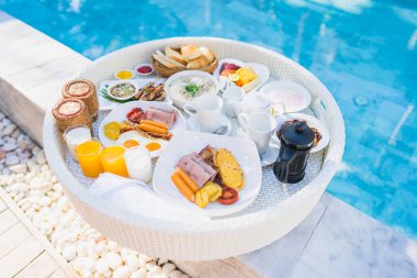 Kızarmış yumurta omletli, jambonlu, meyveli, sütlü kahveli ve yüzme havuzlu bir tepside yüzen kahvaltı.