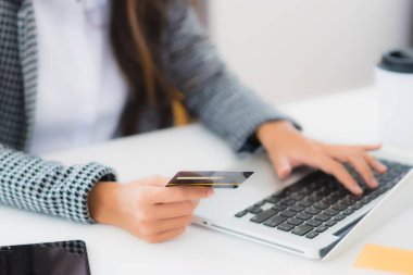 Güzel bir Asyalı kadının portresi online alışveriş malzemesi olarak dizüstü bilgisayarla kredi kartı kullanıyor.