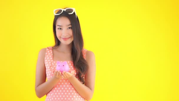 黄色で隔絶された貯金箱を持つ美しいアジア系女性のクローズアップ映像 — ストック動画