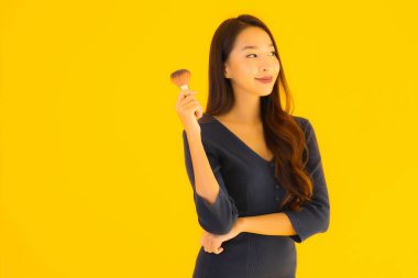 Sarı izole arkaplanda makyaj fırçası olan güzel bir Asyalı kadın portresi.