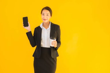 Portre güzel genç Asyalı kadın akıllı cep telefonu ve kahve fincanı ile izole edilmiş sarı arka planda