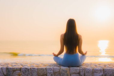 Genç Asyalı kadının portresi sağlık için gün doğumunda deniz kıyısı okyanusunda meditasyon yapıyor.