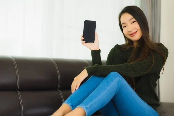 漂亮的年轻亚洲女人在客厅的沙发上使用智能手机或手机 — 图库照片