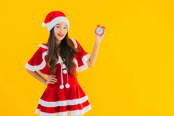 肖像画の美しい若いアジアの女性は クリスマスの服や帽子ショークロックやアラームを身に着けている黄色の隔離された背景 — ストック写真