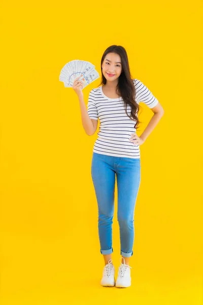 亚洲年轻貌美的女人在黄色的独立背景下表现出大量的美元现金或金钱 — 图库照片