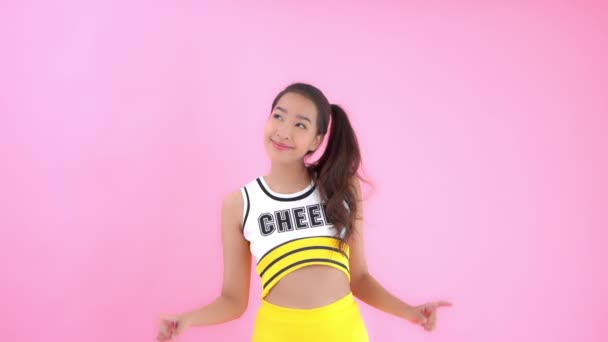 ピンクに隔離されたチアリーディングの制服姿の美しいアジア系女性のクローズアップ映像 — ストック動画