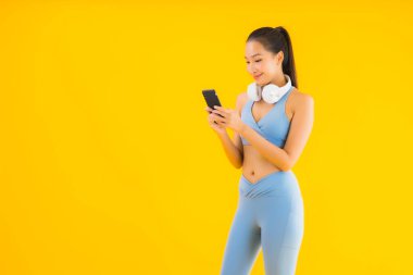 Güzel bir Asyalı kadın portresi. Sarı arka planda müzik dinlemek için akıllı telefon ve kulaklık takıyor.