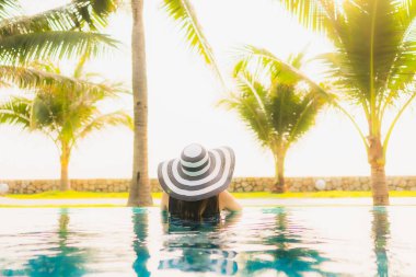 Güzel bir Asyalı kadın portresi, gün batımında palmiye ağacıyla birlikte havuz kenarında dinleniyor ya da tatil için gün doğumunda dinleniyor.