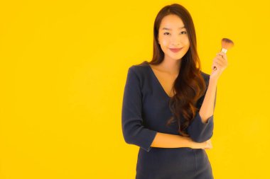 Sarı izole arkaplanda makyaj fırçası olan güzel bir Asyalı kadın portresi.