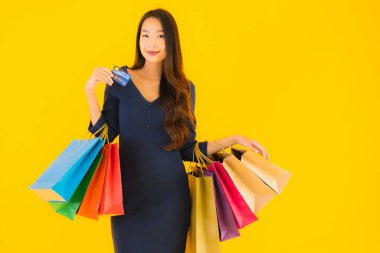 Portre güzel genç Asyalı kadın alışveriş çantası kredi kartı ve akıllı cep telefonu sarısı izole bir arka plan.