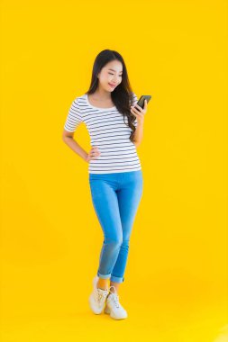 Güzel Asyalı genç bir kadının portresi mutlu bir gülümseme sarı izole edilmiş arka planda akıllı cep telefonu kullanın