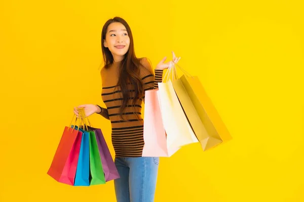 亚洲年轻貌美的女人面带微笑 带着很多色彩的购物袋从百货商店出来 背景是黄色孤立的 — 图库照片