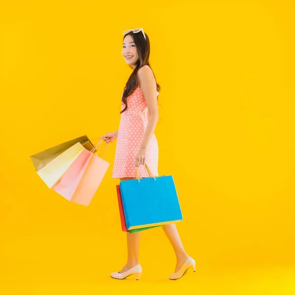 デパートのカラフルなショッピングバッグと黄色の隔離された背景にショッピングモールと肖像画の美しい若いアジアの女性 — ストック写真