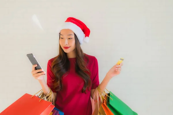 肖像画の美しい若いアジアの女性は ショッピングバッグスマート携帯電話とクレジットカードでクリスマスサンタの帽子を着用 — ストック写真