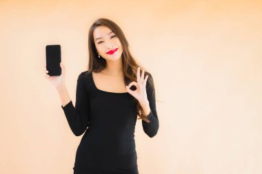 Güzel Asyalı genç bir kadının portresi mutlu bir şekilde gülümsüyor renkli arka planda akıllı cep telefonu kullan