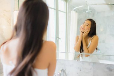 Güzel bir Asyalı kadın portresi. Banyo içerisindeki aynada yüzünü kontrol et ve makyaj yap.