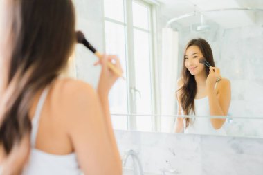 Güzel bir Asyalı kadın portresi. Banyo içerisindeki aynada yüzünü kontrol et ve makyaj yap.