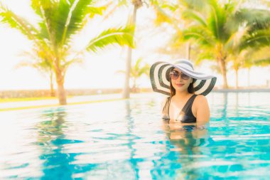 Güzel bir Asyalı kadın portresi, gün batımında palmiye ağacıyla birlikte havuz kenarında dinleniyor ya da tatil için gün doğumunda dinleniyor.