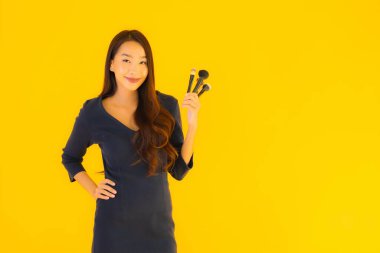 Sarı izole arkaplanda makyaj fırçası olan güzel bir Asyalı kadın portresi.