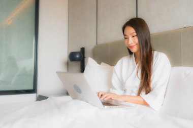 Asyalı güzel bir kadının portresi. Yatak odasının içinde bilgisayar ya da dizüstü bilgisayar kullanıyor.