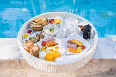 Kızarmış yumurta omletli, jambonlu, meyveli, sütlü kahveli ve yüzme havuzlu bir tepside yüzen kahvaltı.