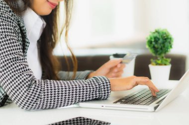Güzel bir Asyalı kadının portresi online alışveriş malzemesi olarak dizüstü bilgisayarla kredi kartı kullanıyor.