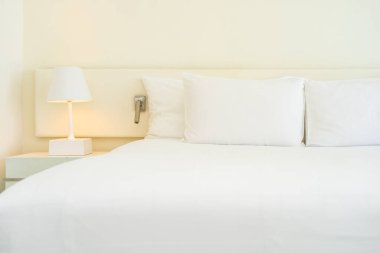 Yatak odasının içinde lamba süslemesi olan beyaz rahat yastık ve battaniye.