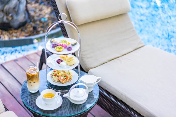 Afternoon tea set with latte coffee and hot tea on table neary chair around swimming pool in hotel resort