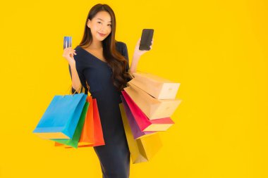 Portre güzel genç Asyalı kadın alışveriş çantası kredi kartı ve akıllı cep telefonu sarısı izole bir arka plan.