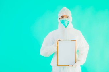 Güzel, genç Asyalı doktor kadın koronavirüsten korunmak için ppe ya da kişisel koruyucu ekipman takıyor ya da mavi izole arka planda beyaz kartı olan 19. bölgede yaşıyor.