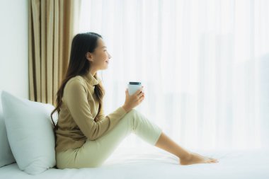 Yatak odasının iç tarafında, kahve fincanı olan Asyalı genç bir kadın.