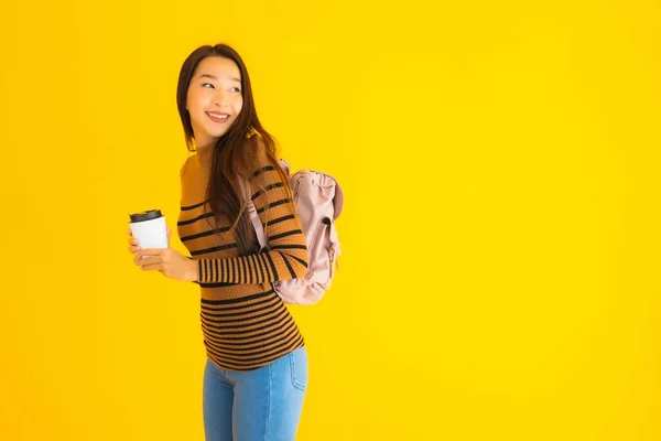 ポートレート美しいです若いですアジアの女性とともにBagpackとコーヒーカップ上の彼女の手で黄色隔離された背景 — ストック写真