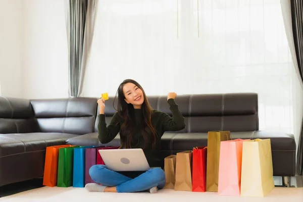 ポートレート美しい若いアジアの女性は自宅でオンラインショッピングのためのショッピングバッグとラップトップとクレジットカードを使用しています — ストック写真