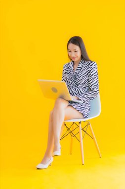 Güzel bir Asyalı kadın, sarı izole edilmiş arka planda dizüstü bilgisayar kullanıyor.