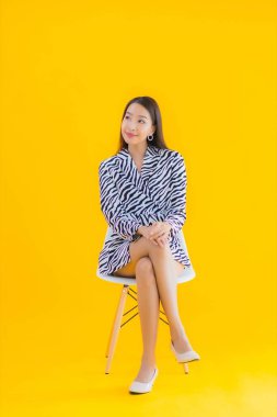 Güzel bir Asyalı kadın, sarı izole edilmiş arka planda hareketli bir şekilde sandalyede oturuyor.