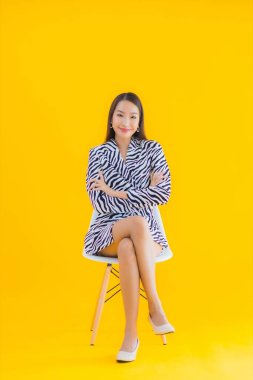 Güzel bir Asyalı kadın, sarı izole edilmiş arka planda hareketli bir şekilde sandalyede oturuyor.