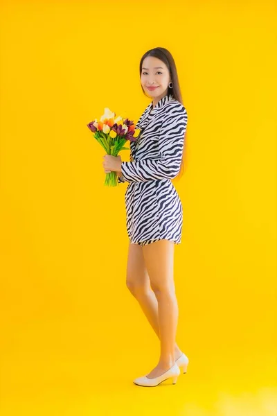 年轻美丽的亚洲女子在黄色的孤零零的背景上 为花朵的绽放而高兴 — 图库照片