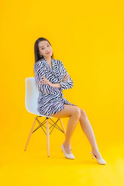 Portrait beautiful young asian woman sit on chair with action on yellow isolated background