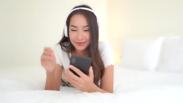 美丽的年轻亚洲女人在家用耳机和智能手机听音乐的镜头 — 图库视频影像