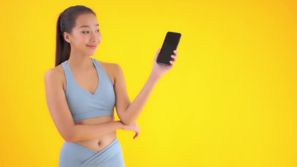 美丽的年轻亚洲女人带着智能手机穿着啦啦队队长制服与黄色隔离的镜头 — 图库视频影像