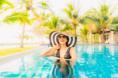 Güzel bir Asyalı kadın portresi, gün batımında palmiye ağacıyla birlikte havuz kenarında dinleniyor ya da tatil için gün doğumunda dinleniyor.