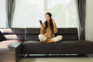 Güzel bir Asyalı kadın portresi. Müzik dinlemek için kulaklıkla akıllı telefon ya da cep telefonu kullanıyor.
